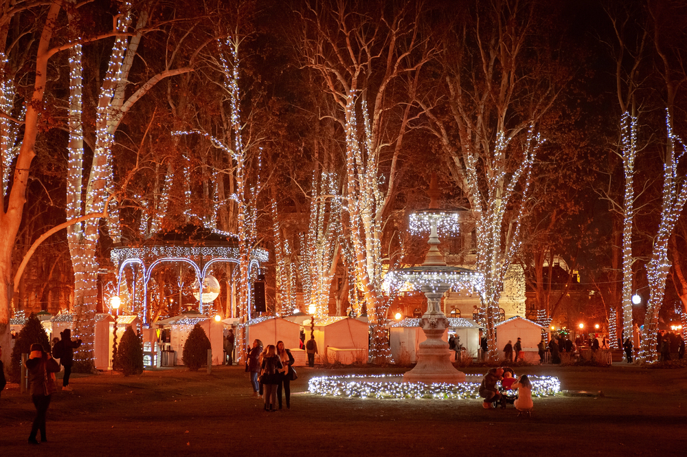 Pohled na kašnu a a altánek v parku, které jsou ozdobené vánočními světýlky.